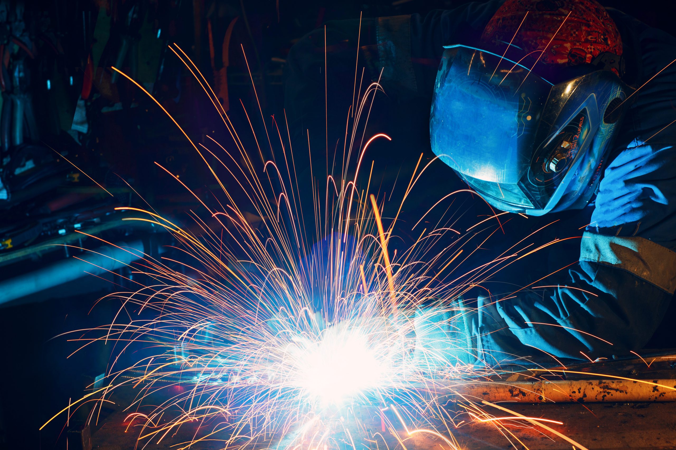 Welder welding metal construction on factory. Long traces of sparks